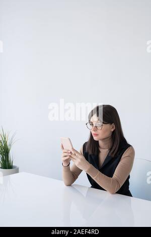 Pretty young businesswoman in smart casual scrolling in smartphone by desk Stock Photo