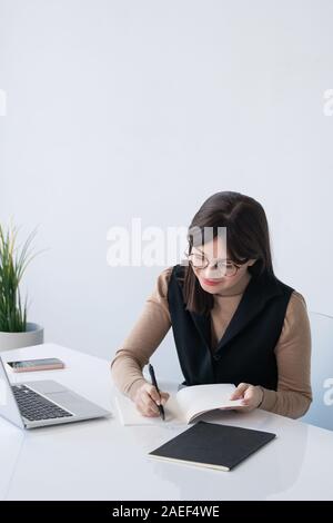 Young successful businesswoman writing down plan of working day by desk Stock Photo