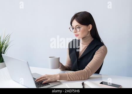 Young serious businesswoman with mug analyzing online financial data Stock Photo