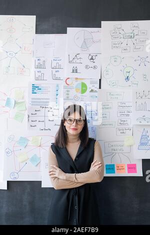 Young economist standing by blackboard with flow charts and diagrams on papers Stock Photo