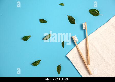 Two wooden bamboo eco friendly toothbrushes, green leaf, white towel on blue background. Eco friendly, reuse and valentines day concept. Flat lay, top Stock Photo
