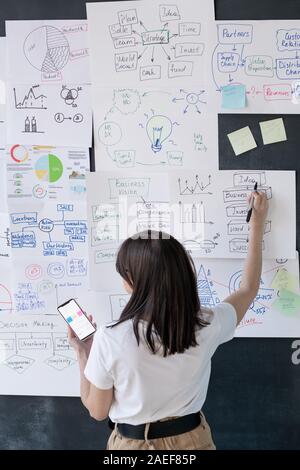 Back view of female coach with smartphone pointing at financial information Stock Photo
