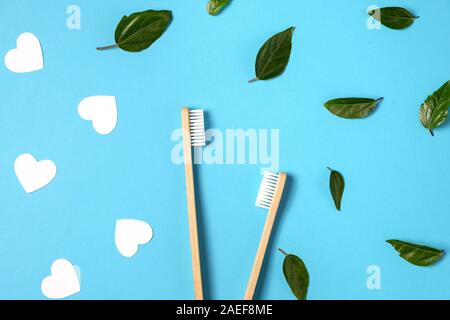 Two wooden bamboo eco friendly toothbrushes, green leaf, white heart on blue background. Dental care, eco friendly, reuse and valentines day concept. Stock Photo