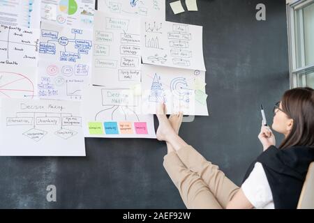 Young barefoot businesswoman sitting in front of blackboard and analyzing data Stock Photo