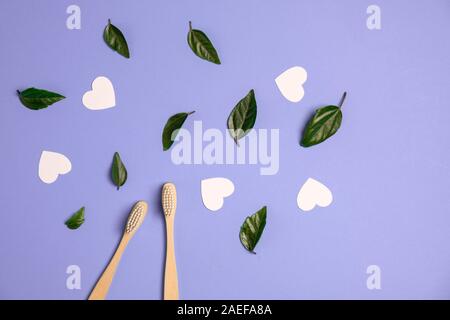Zero waste concept. Two wooden bamboo eco friendly toothbrushes, green leaf, white hearts on purple background. Eco friendly, valentines day concept. Stock Photo