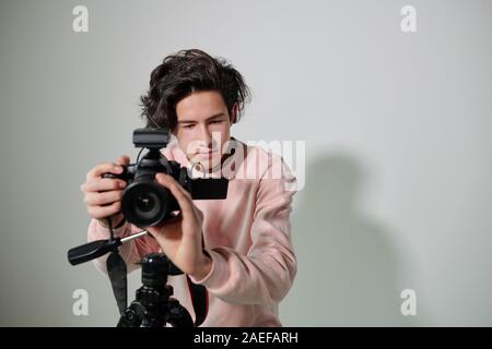Young cameraman in powdery pink sweatshirt regulating video equipment Stock Photo