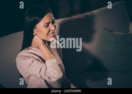 Close-up portrait of her she nice attractive sick sad brunet girl sitting on divan suffering from muscle ache spasm touching neck at night late Stock Photo