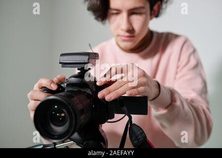 Hands of young cameraman in powdery pink sweatshirt regulating video equipment Stock Photo