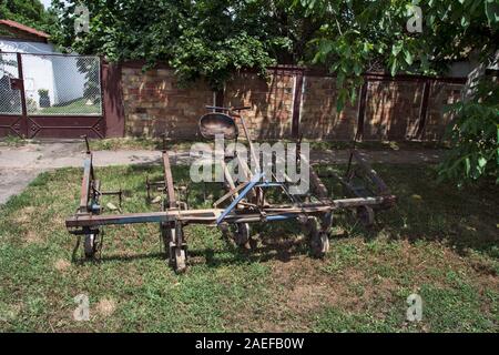 An old farm machine used to plow the fields stands in front of the farmhouse. Memories of old times gone by. Stock Photo