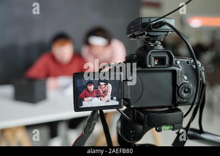 Two young contemporary male vloggers on screen of video camera in studio Stock Photo