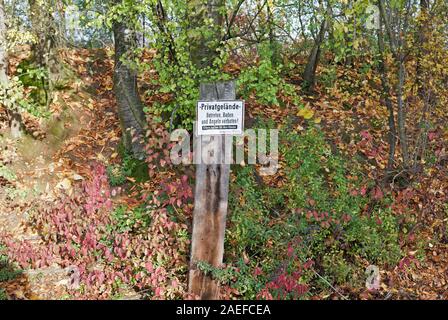 Private Property, no trespassing bathing or fishing sign, mounted on wooden plank, German, Autumn leaves on ground, bushes trees in background,Germany Stock Photo