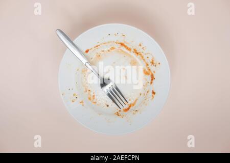 A plate with rests of tomato sauce in it, top view. Unwashed dishes illusatration, filthy plate on light background Stock Photo