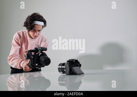 Young serious video blogger standing in front of new photo equipment on desk Stock Photo