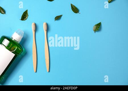 Oral care products. Mouthwash, two wooden bamboo eco friendly toothbrushes, green leaf on blue background. Teeth hygiene concept. Flat lay, copy space Stock Photo