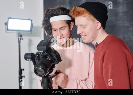 Two happy young males watching recorded video on digital screen of camera Stock Photo