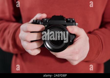 Hands of young male photographer in maroon sweatshirt holding new photocamera
