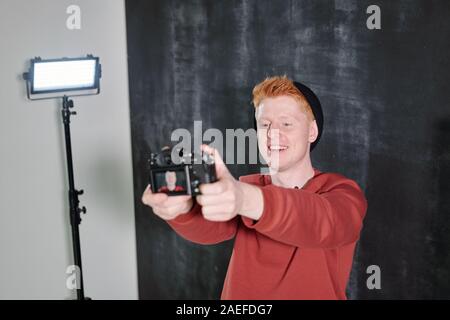 Cheerful young vlogger in casualwear holding camera in front of himself Stock Photo