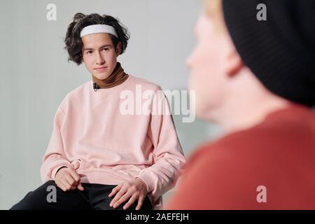 Serious man in powdery pink pullover and white headband interacting with vlogger Stock Photo