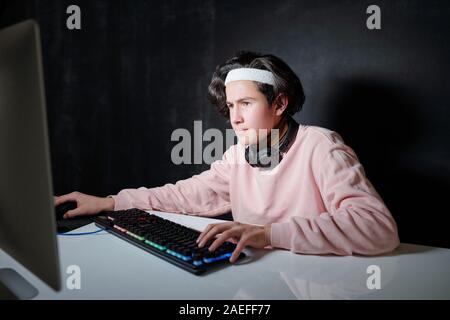 Serious guy with headphones around neck concentrating on network in dark room Stock Photo