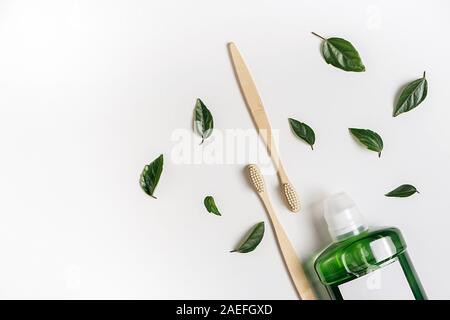 Mouthwash, two wooden bamboo eco friendly toothbrushes, green leaf on white background. Teeth hygiene concept. Flat lay, copy space Stock Photo