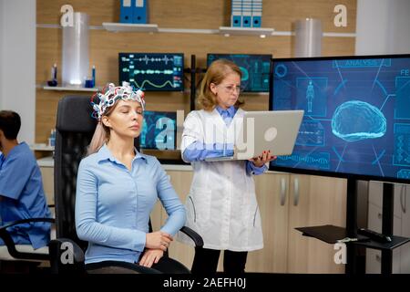 Doctor analyzing live data on a laptop during a girl's brain scan procedure. Brain waves scanning device Stock Photo