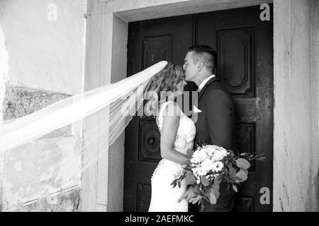 The kiss. Groom kisses bride on forehead in front of church portal. Stock Photo