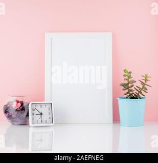 Blank white frame, clock and plant cactus on a white table against the pink wall. Mockup with copy space. Stock Photo
