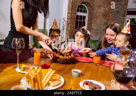 Portrait of happy multiethnic family celebrating a birthday at home. Big family eating cake and drinking wine while greeting and having fun children. Celebration, family, party, home concept. Stock Photo