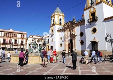 Tourists relaxing by the Hercules Fountain with the Socorro church to the rear in the Socorro Plaza, Ronda, Malaga Province, Spain. Stock Photo