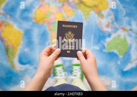 Child's hand holding US passport. Map background. Ready for traveling. Open world. Stock Photo