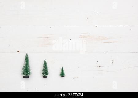 Top view on three little Christmas trees on white wooden background. Holidays and winter concept. Stock Photo