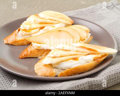 Plate with three delicious French toast with a bananas, pears, cream cheese, caramel syrup, side view, gray table. Stock Photo