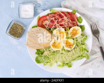 Diet salad with soft boiled eggs, salt, cheese and the vegetables - tomatoes, lettuce. Blue light background, top view. Stock Photo