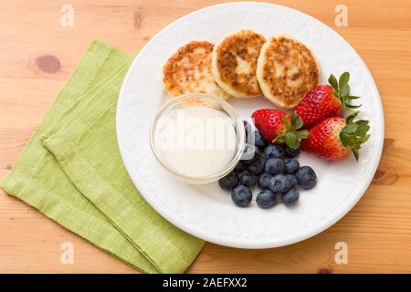 Top view on white plate with cakes made of cottage cheese with blueberries, strawberries and sweet sause on wooden table. Healthy snack. Breakfast ide Stock Photo