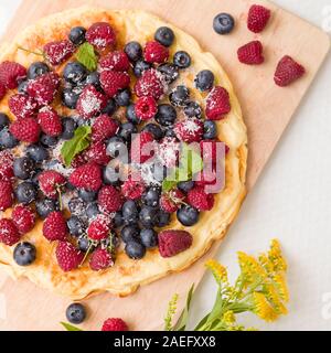 Fresh berries on the tart cake from above. Delicious homemade pie with organic raspberries and blueberries and summer flowers on wooden board. Summer Stock Photo