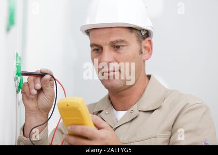 happy electrician checking voltage in electrical wall socket Stock Photo