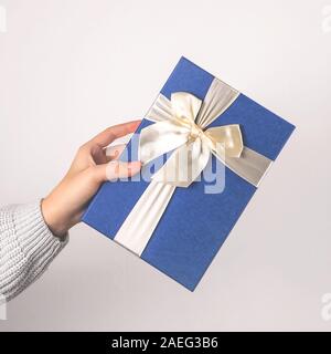 Big blue gift box with a light ribbon and bows in female hands. Preparing for Christmas concept. Stock Photo