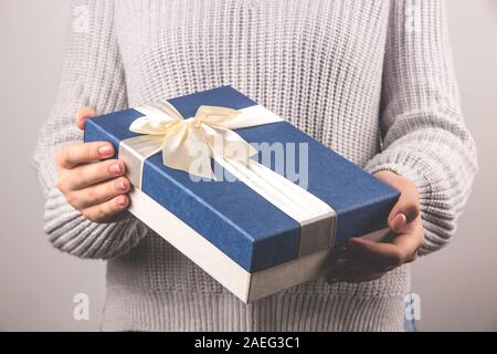 Big blue gift box with a light ribbon and bows in female hands. Preparing for Christmas concept. Stock Photo