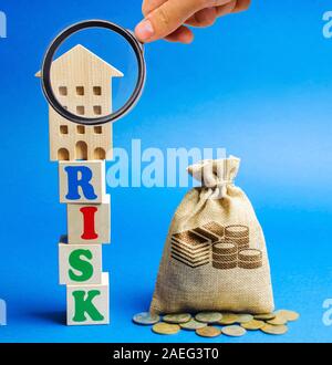 Wooden blocks with the word Risk and a miniature house with a money bag. Real estate investment risk. Risky investments. Loss of property for non-paym Stock Photo