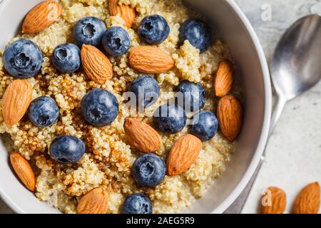 Healthy quinoa porridge with blueberries and almonds with syrup in gray bowl. Vegan food concept. Stock Photo