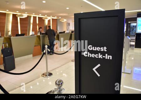 Guest check in sign at Hilton Metropole in London with blurred background showing unidentifiable staff checking in guests with bags and suitcases Stock Photo
