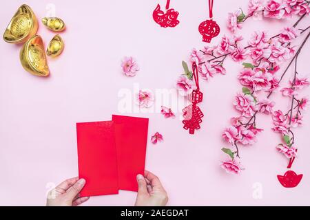 Flat lay Chinese lunar new year hand offering red envelope on pink background, Translation of text appear in image: Prosperity, rich and healthy. Stock Photo