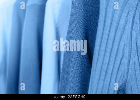 Row of knitted warm sweaters onhangers toned blue color. Stock Photo