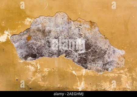 yellow plaster on a house wall which has a crack and crumbles off as a background Stock Photo