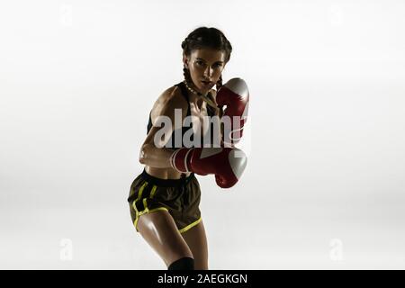 Fit caucasian woman in sportswear boxing isolated on white studio background. Novice female caucasian boxer training and practicing in motion and action. Sport, healthy lifestyle, movement concept. Stock Photo