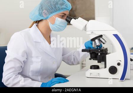 Young medical worker looking on samples through microscope Stock Photo