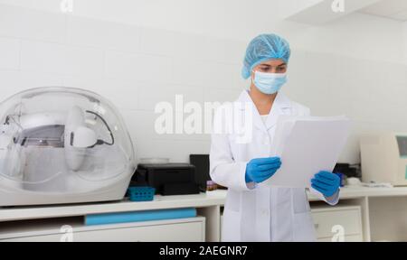 Cheerful assistant in protective mask and gloves reading safety regulations in lab Stock Photo