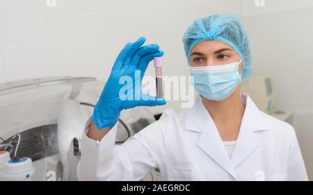 Young female in mask and gloves preparing blood samples for making diagnostic Stock Photo