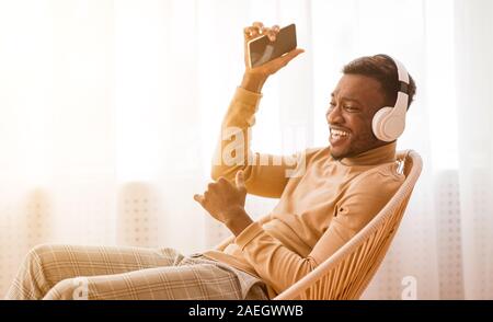 Joyful Guy In Headphones Using Cellphone Listening Music At Home Stock Photo