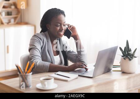 Busy Black Businesswoman Working In Office With Smartphone And Laptop. Stock Photo